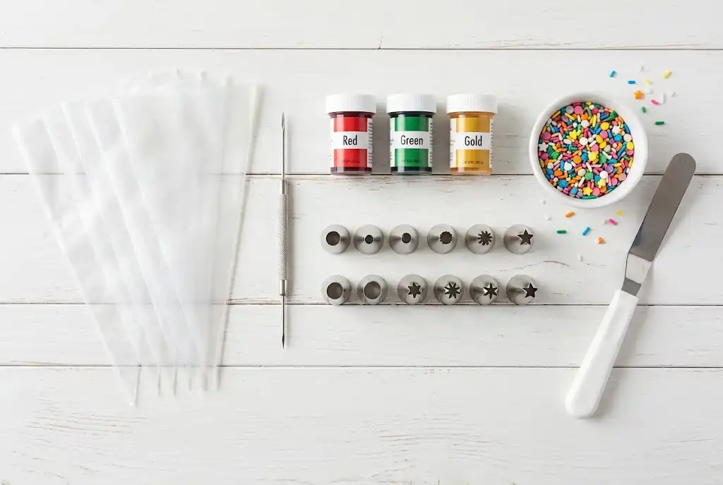 Flat-lay photo of essential cookie decorating tools including tipless bags, scribe tool, gel colors, and piping tips
